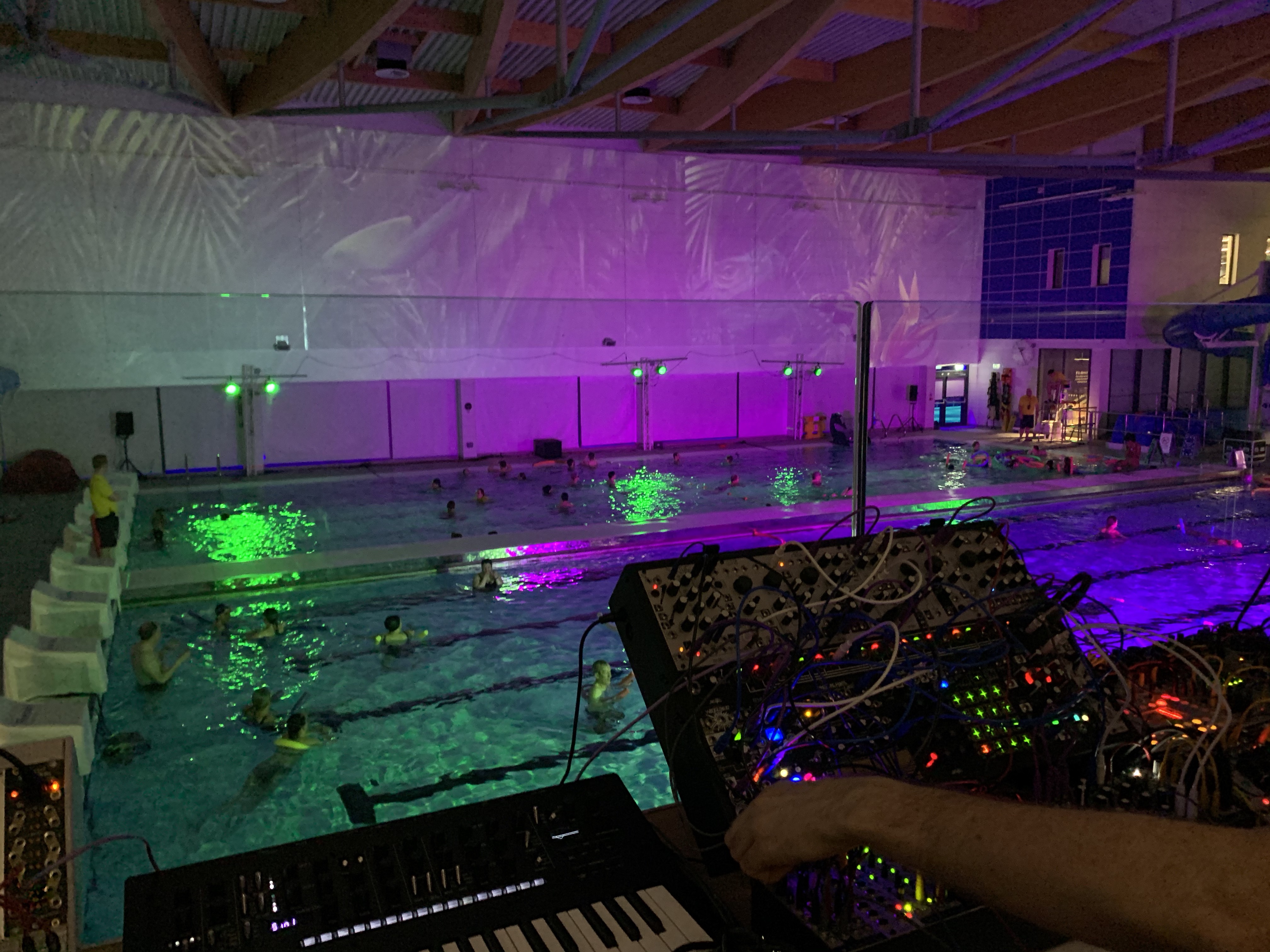Two synthesisers being played pool side in a neon illuminated swimming pool.